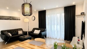 Un salon moderne avec une table à manger en bois, deux canapés, un téléviseur et une grande fenêtre avec des rideaux.