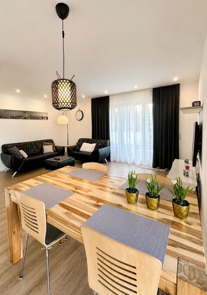 Un salon moderne avec une table à manger en bois, deux canapés, un téléviseur et une grande fenêtre avec des rideaux.