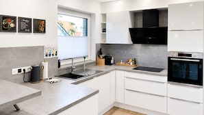 Une cuisine moderne avec des meubles blancs, une hotte noire et un four encastré.