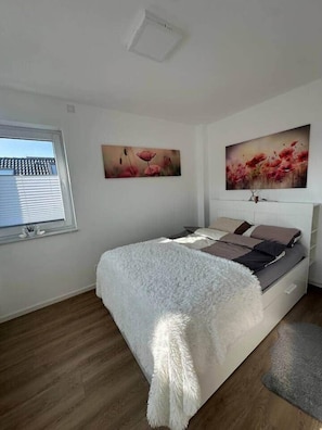 A bedroom with a bed, a window, and two wall-mounted paintings.