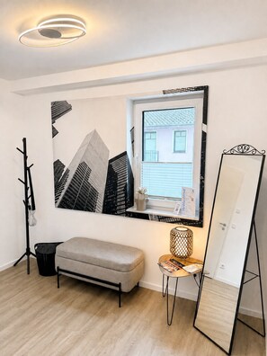 Une pièce au design moderne, agrémentée d’une grande œuvre d’art représentant un paysage urbain encadré, d’un banc, d’une petite table avec une lampe et d’un grand miroir.
