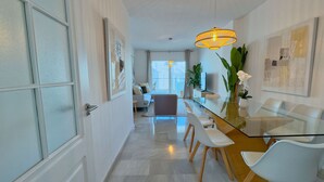 A modern living room with a sofa, chairs, a glass dining table, and a large window. - Beachfront Apartment with Swimming Pools (Mijas Costa)