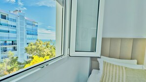 A hotel room with a bed, a window, and a view of a building and trees. - Beachfront Apartment with Swimming Pools (Mijas Costa)