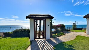 A coastal property with a thatched-roof gate, a paved pathway, and a bench by the sea. - Beachfront Apartment with Swimming Pools (Mijas Costa)