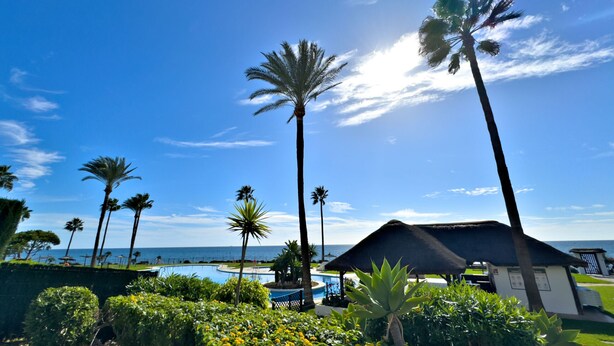 A resort with a pool, palm trees, and a view of the ocean. - Beachfront Apartment with Swimming Pools (Mijas Costa)