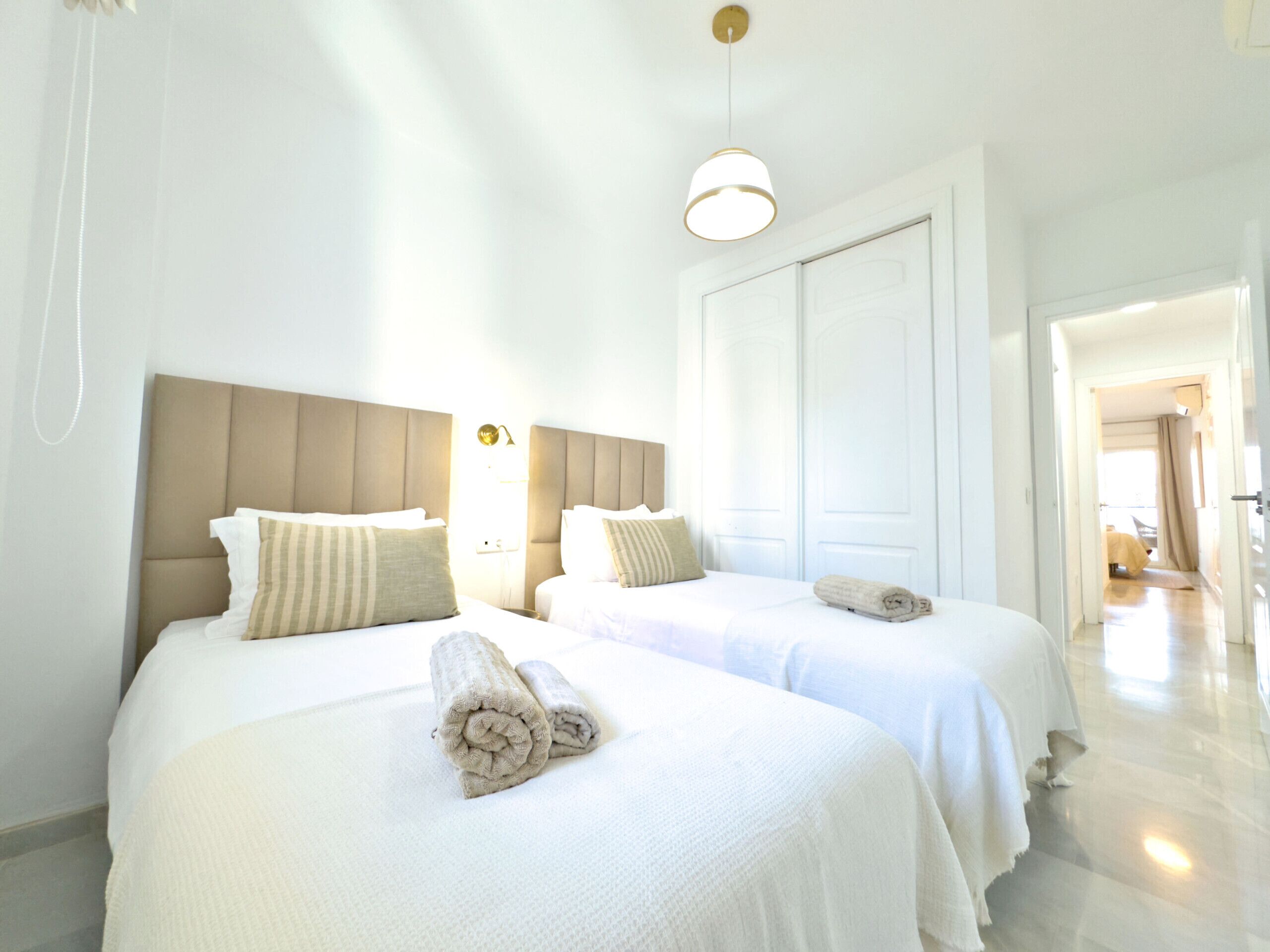 Hotelkamer met twee bedden, elk voorzien van een hoofdeinde, een bedlampje en een opgerolde handdoek op het bed.