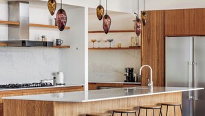 Une cuisine moderne dotée d’un grand îlot central, d’appareils électroménagers en acier inoxydable, de meubles en bois et de luminaires suspendus.