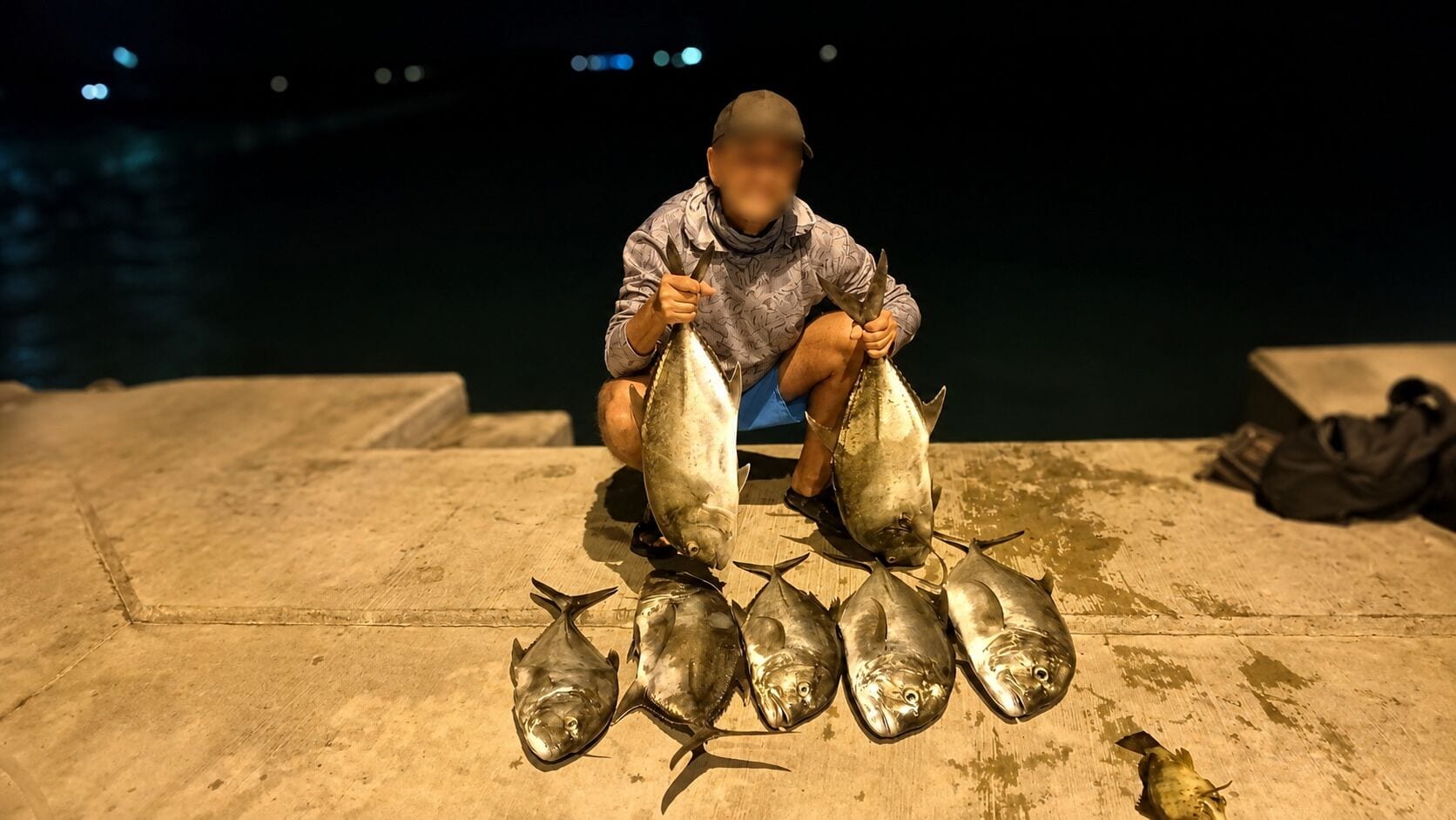 Eine Person hält zwei große Fische auf einer Betonfläche.