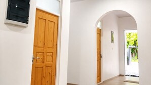 A hallway with a wooden door, a trash bin, and a wall-mounted device. - Bon Abri maldives (Magoodhoo)