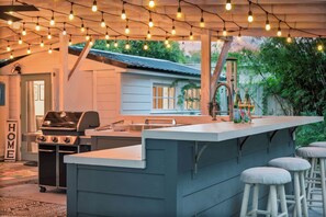 An outdoor kitchen area with a built-in bar, bar stools, and string lights. - Spacious 3BR w/ MIL suite & backyard (Orlando)