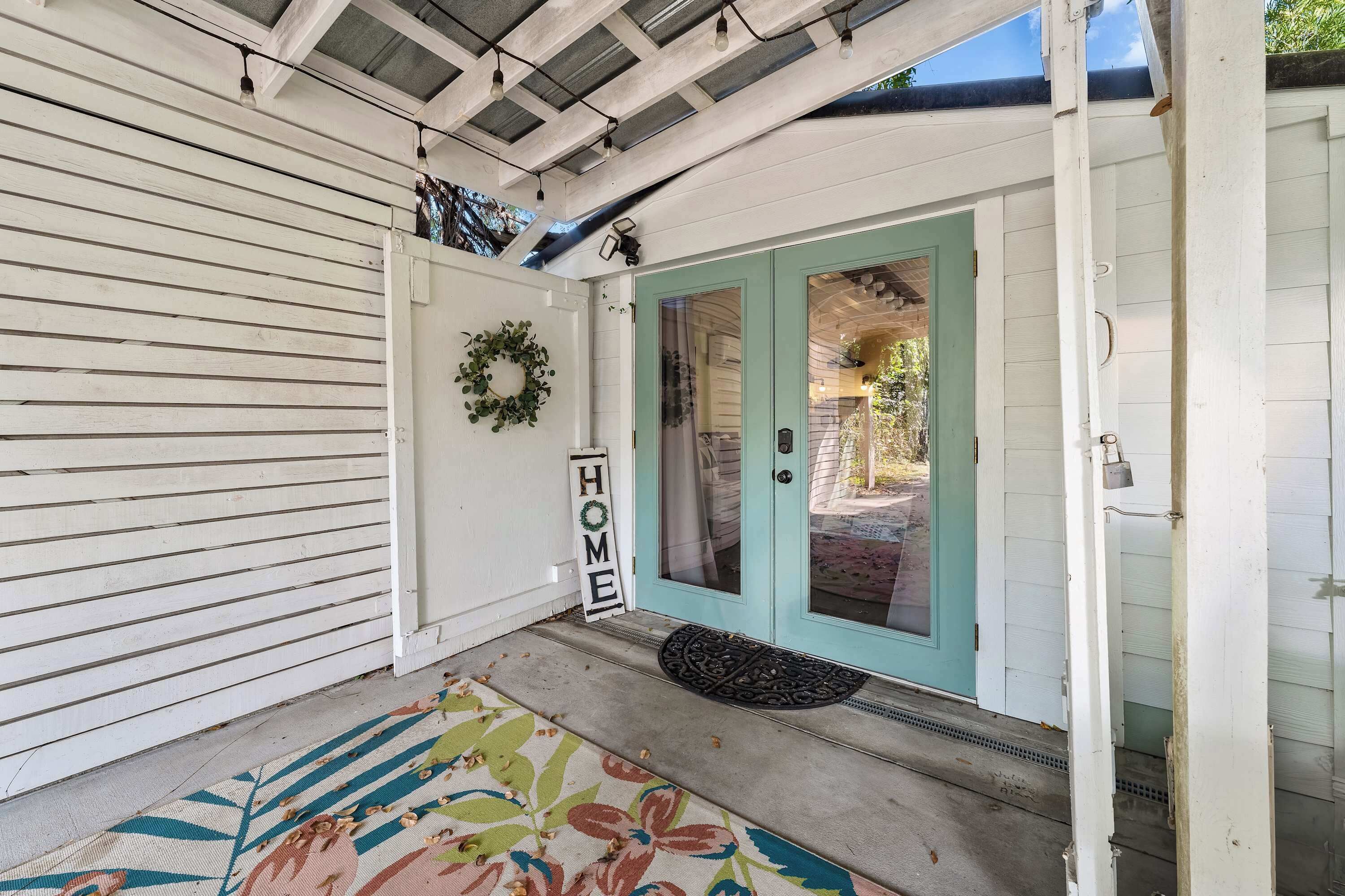 Un porche avec une porte de couleur turquoise, une enseigne portant l’inscription « HOME » et un paillasson.