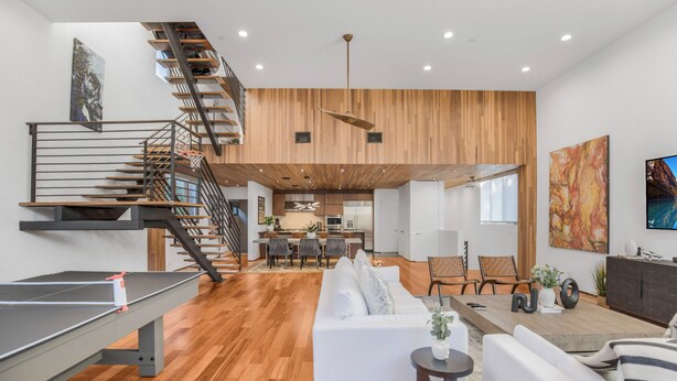 A spacious living area with a wooden floor, a white sofa, a dining table, and a staircase leading to an upper level. - Cedar Loft Villa (Venice)