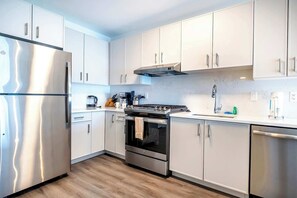 A modern kitchen with white cabinets, stainless steel appliances, and a wooden floor.