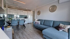 A modern living room with a grey sofa, a dining table with chairs, and a kitchen area in the background. - SUNSET VIEW HILL (Costa Adeje)