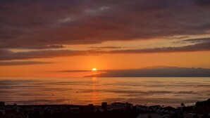A sunset over a calm sea with distant mountains, and a silhouette of buildings in the foreground. - SUNSET VIEW HILL (Costa Adeje)