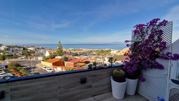 A balcony with a view of a coastal town, potted plants, and a white lattice fence. - SUNSET VIEW HILL (Costa Adeje)