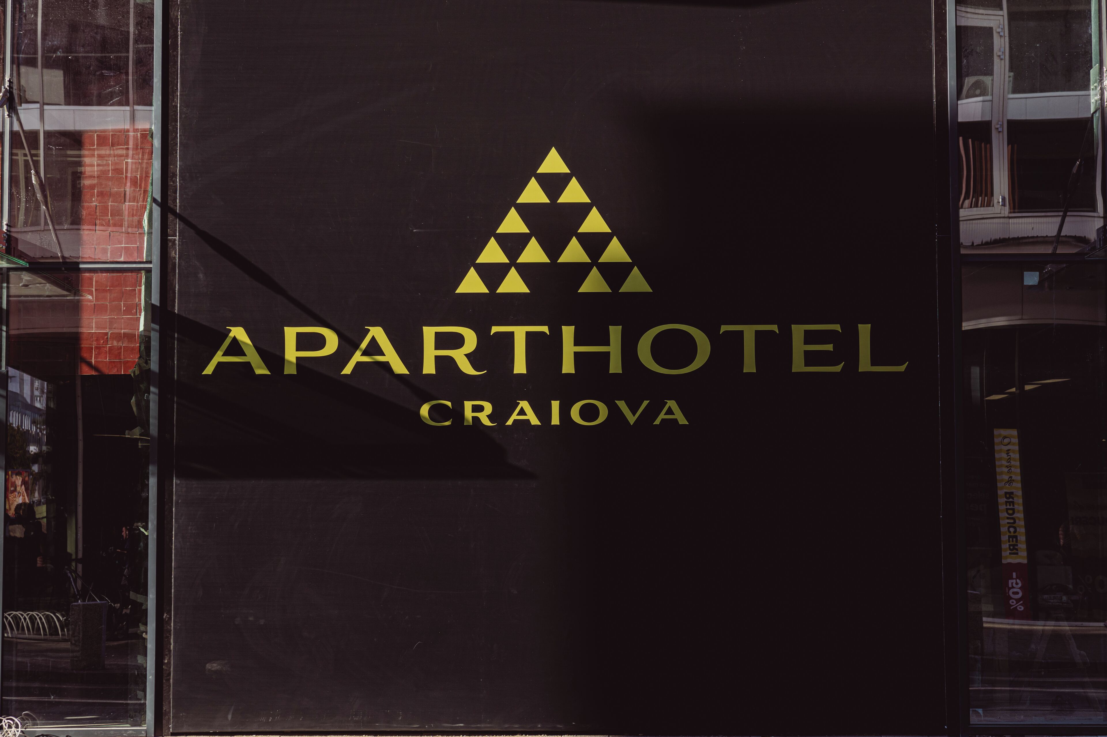 Une enseigne pour l’hôtel-résidence Aparthotel Craiova, avec un logo triangulaire et le nom écrit en lettres dorées.