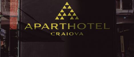 Une enseigne pour l’hôtel-résidence Aparthotel Craiova, avec un logo triangulaire et le nom écrit en lettres dorées.