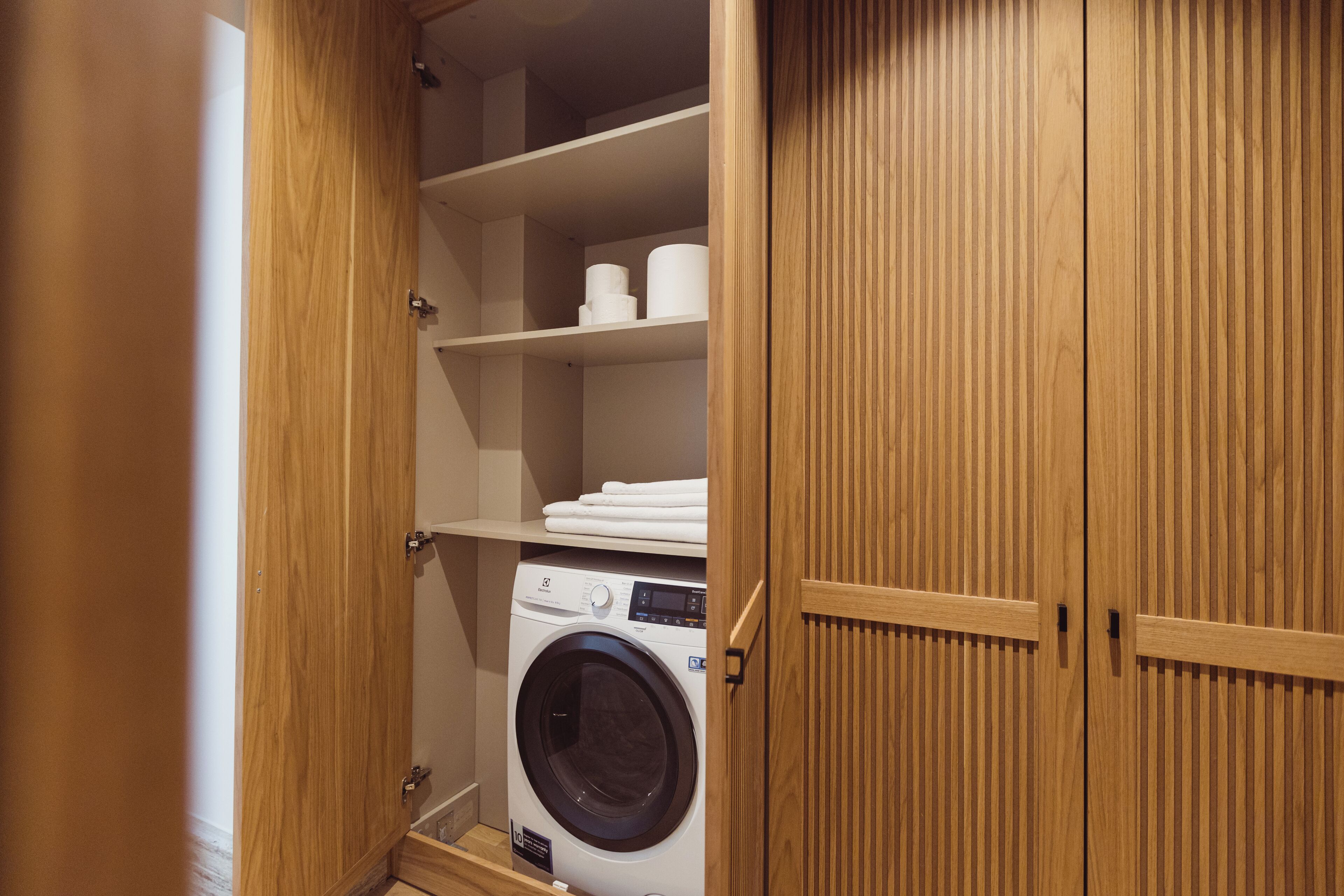 Un cuarto de lavado con lavadora, repisas con toallas y puertas de madera.