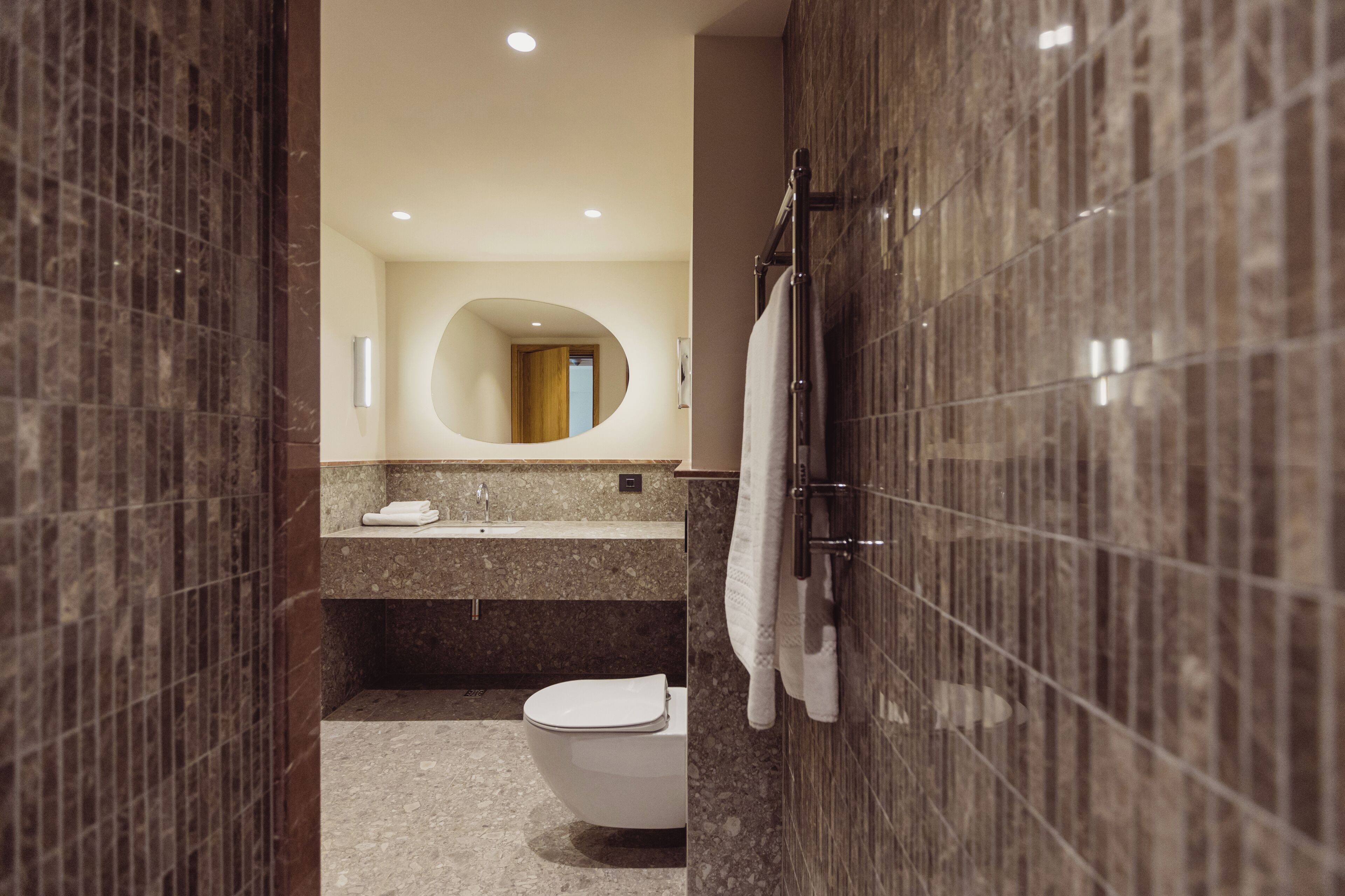 A modern bathroom with a marble sink, a toilet, and a towel rack.