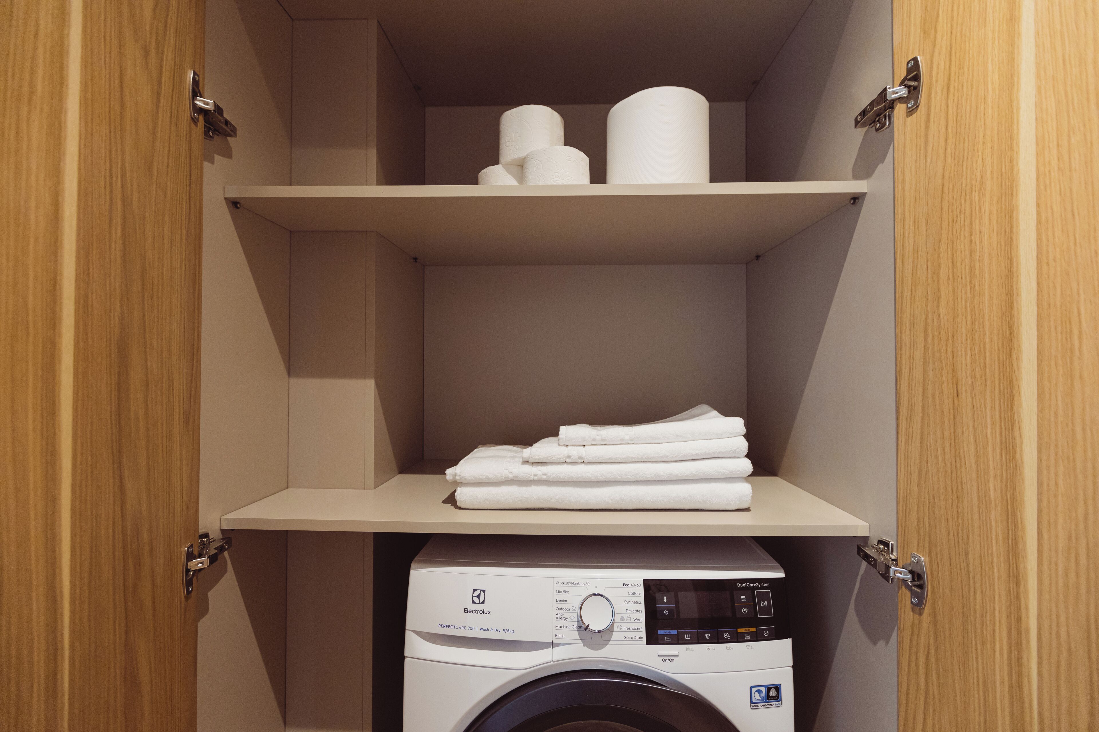 A laundry room with a washing machine and neatly folded towels on a shelf.