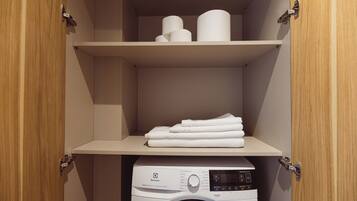 A laundry room with a washing machine and neatly folded towels on a shelf.