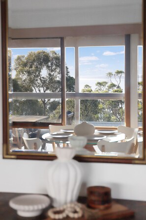 A room with a large window, a table with chairs, and a vase. - Seaview Cottage (Lorne)