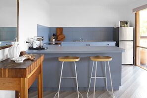 A modern kitchen with a central island, bar stools, a refrigerator, and a microwave. - Seaview Cottage (Lorne)