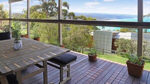 A wooden deck with a table and chairs, potted plants, and a view of a coastal landscape.