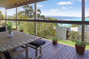 A wooden deck with a table and chairs, potted plants, and a view of a coastal landscape.