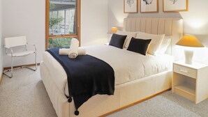 A hotel room with a bed, bedside table, lamp, chair, and artwork on the wall.