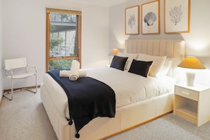 A hotel room with a bed, bedside table, lamp, chair, and artwork on the wall.