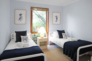 A room with two single beds, a nightstand with a lamp, and framed artwork on the walls. - Seaview Cottage (Lorne)