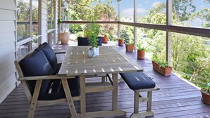 A wooden deck with a table and chairs, surrounded by potted plants and large windows.