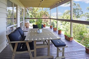 A wooden deck with a table and chairs, surrounded by potted plants and large windows.