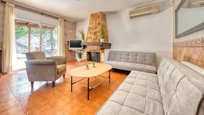 Ein Wohnzimmer mit Kamin aus Stein, einem grauen Sofa, einem runden Couchtisch und einem Fernseher.