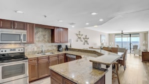 A modern kitchen with granite countertops, stainless steel appliances, and wooden cabinets. - Summerchase 704 by Liquid Life (Orange Beach)
