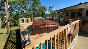 Une terrasse en bois avec un jacuzzi, une lanterne et un espace abrité aménagé avec du mobilier d’extérieur.