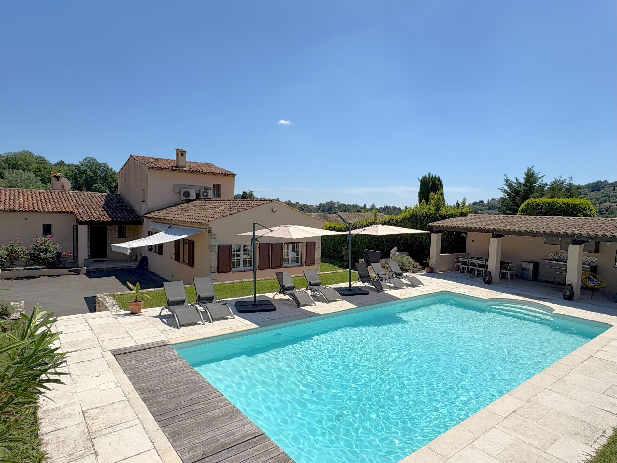 Une piscine entourée de bâtiments aux toits couverts de tuiles, avec des chaises longues et des parasols à proximité.