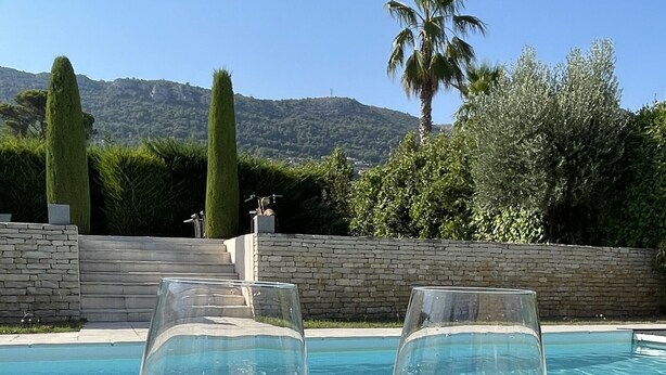 Deux verres à vin sont posés sur une table près d’une piscine, avec une vue sur les montagnes en arrière-plan.