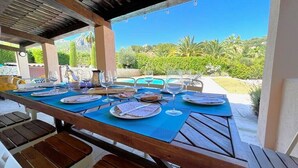 Un espace de restauration en plein air avec une table en bois dressée pour un repas, entourée de chaises et offrant une vue sur la verdure et un ciel dégagé.