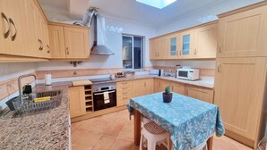 A compact kitchen with wooden cabinets, a built-in oven, a microwave, and a small dining area with a table and chairs. - Cozy Townhouse, quiet location, near the river and outdoor space (Estômbar)