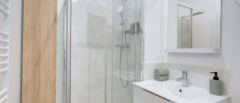 Un baño moderno con ducha de vidrio, lavamanos blanco y espejo superior.