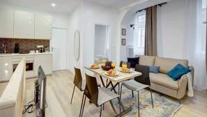 A modern living room with a sofa, a dining table with breakfast items, and a kitchen area with cabinets and a TV. - Charming 1BR in Montorgueil - Les Halles (Paris)