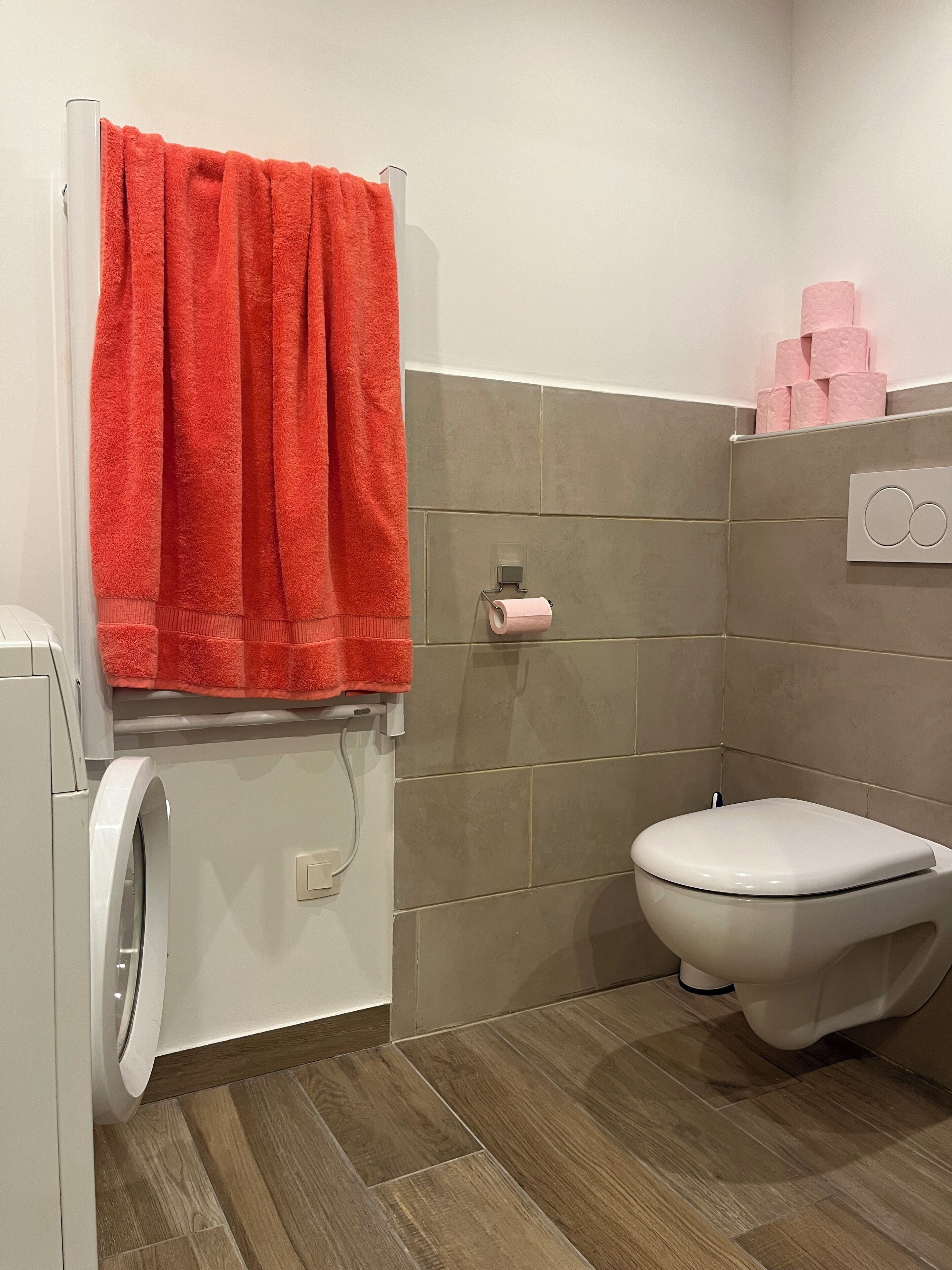 A bathroom with a washing machine, a toilet, and a towel rack with a red towel.