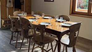 Un comedor con una mesa de madera dispuesta para seis personas, rodeada de sillas de madera. Se ve un perchero con objetos colgados a la izquierda.