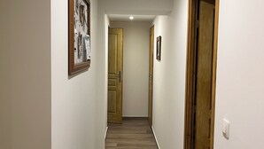 Un pasillo estrecho con suelo de madera, paredes blancas y dos puertas de madera al final.