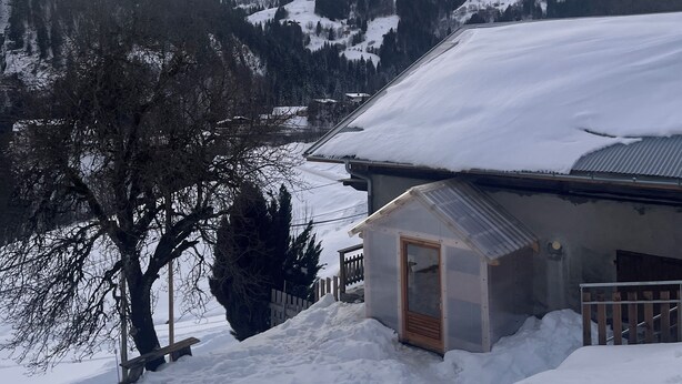 Un paisaje nevado de montaña con un edificio que tiene una puerta de madera y un techo de metal.