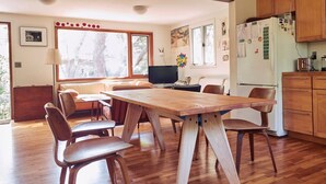 A spacious kitchen with wooden flooring, a large dining table, and wooden chairs. There is a television and a refrigerator in the kitchen. - Quiet, cozy home in the woods CS0038 (Wellfleet)
