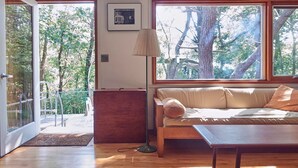 A cozy room with a wooden floor, a sofa with cushions, a lamp, and a picture on the wall. - Quiet, cozy home in the woods CS0038 (Wellfleet)